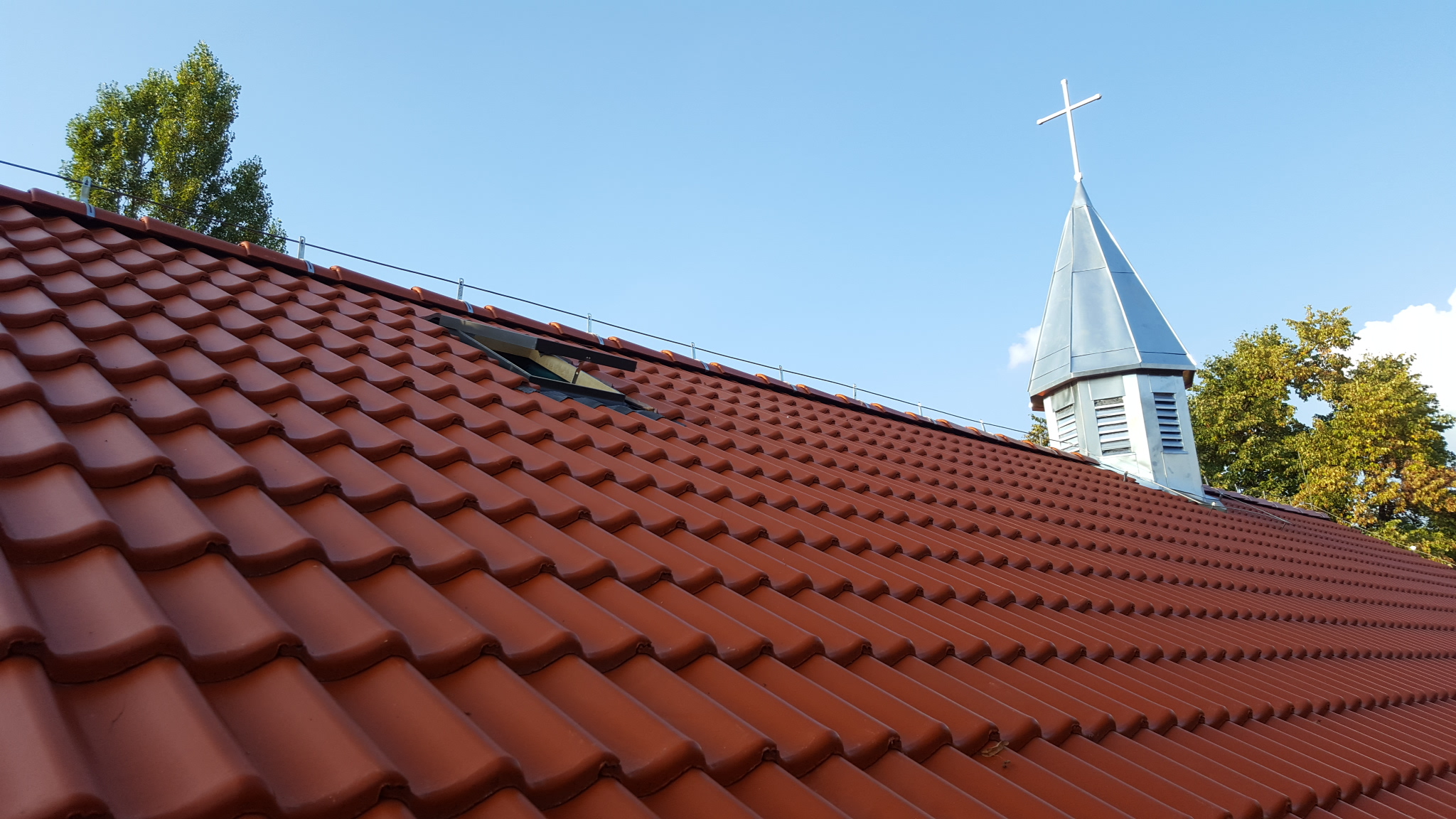Dach kościoła z dachówką i wieżą z krzyżem